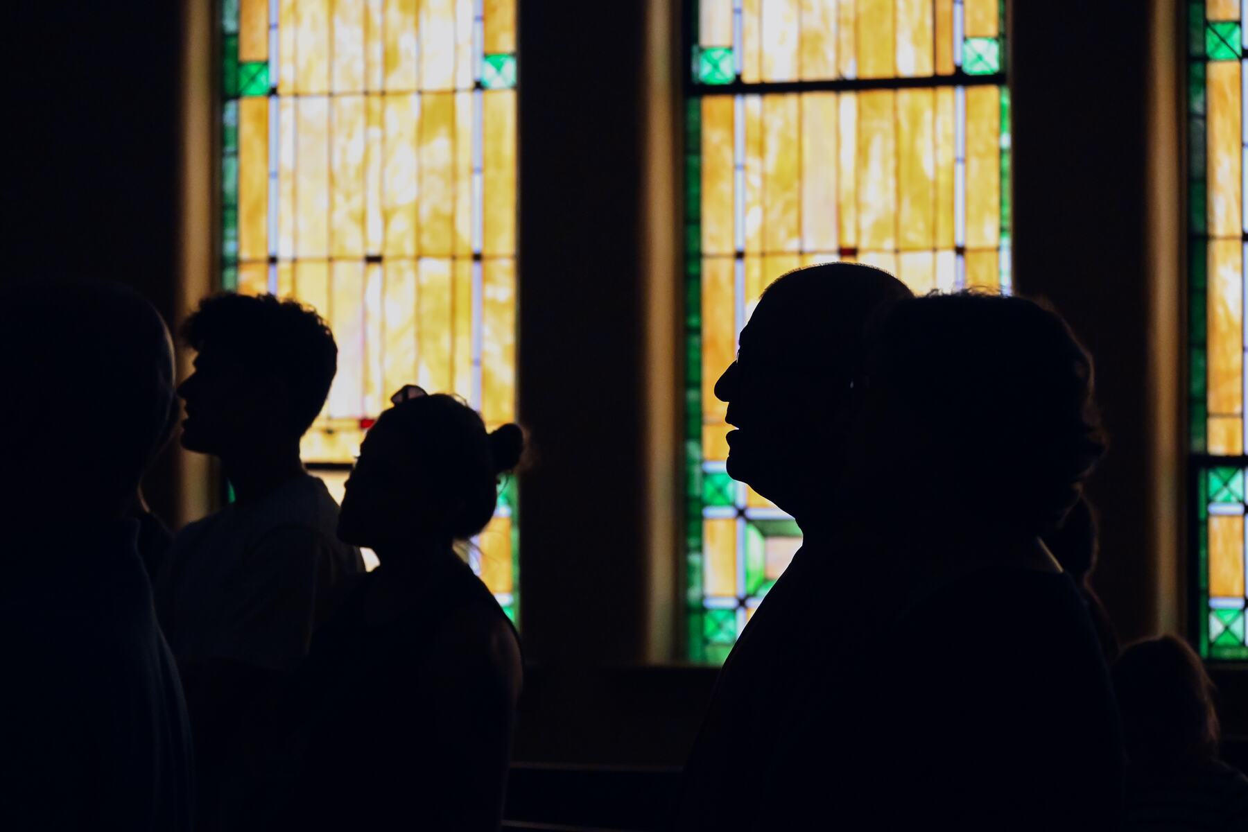 Worshippers in silhouette against the sanctuary's stained-glass windows.